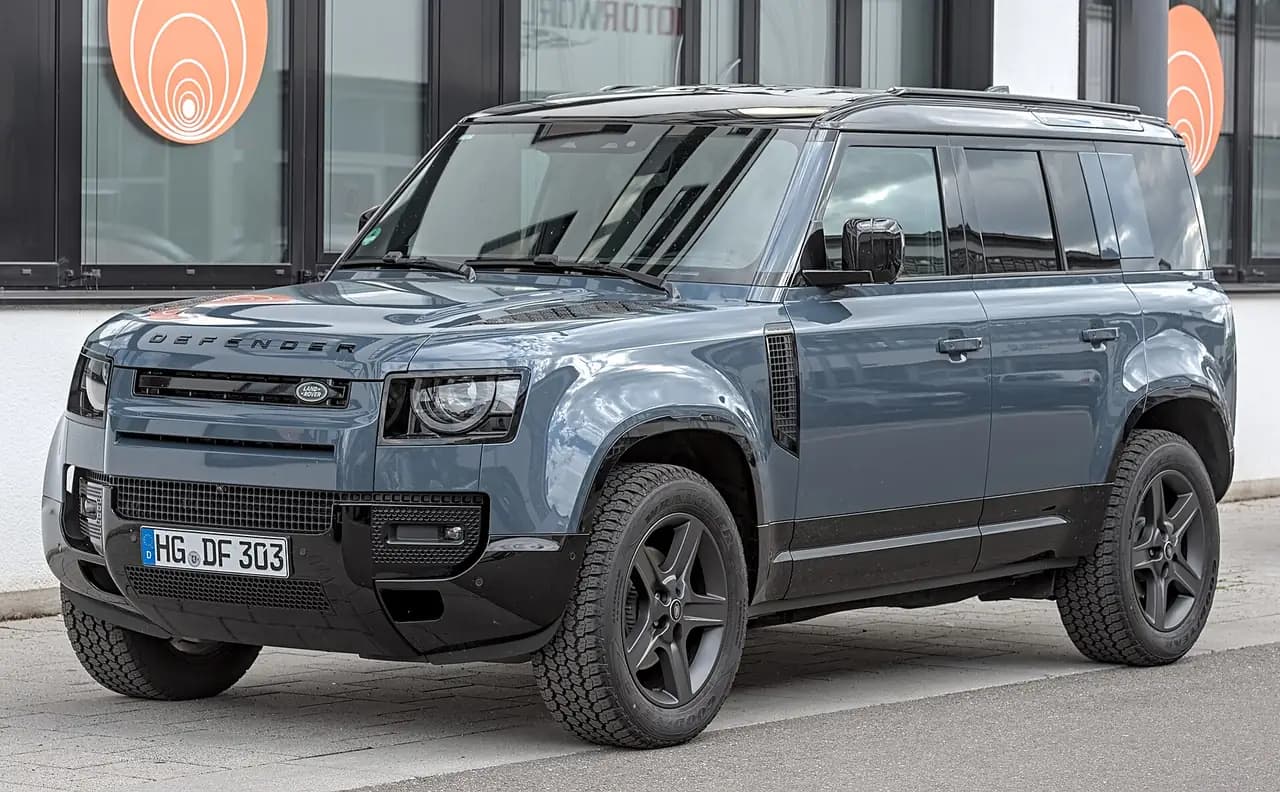 Blue-grey Land Rover Defender 110 (L663) with black wheels and all-terrain tyres, front three-quarter view
