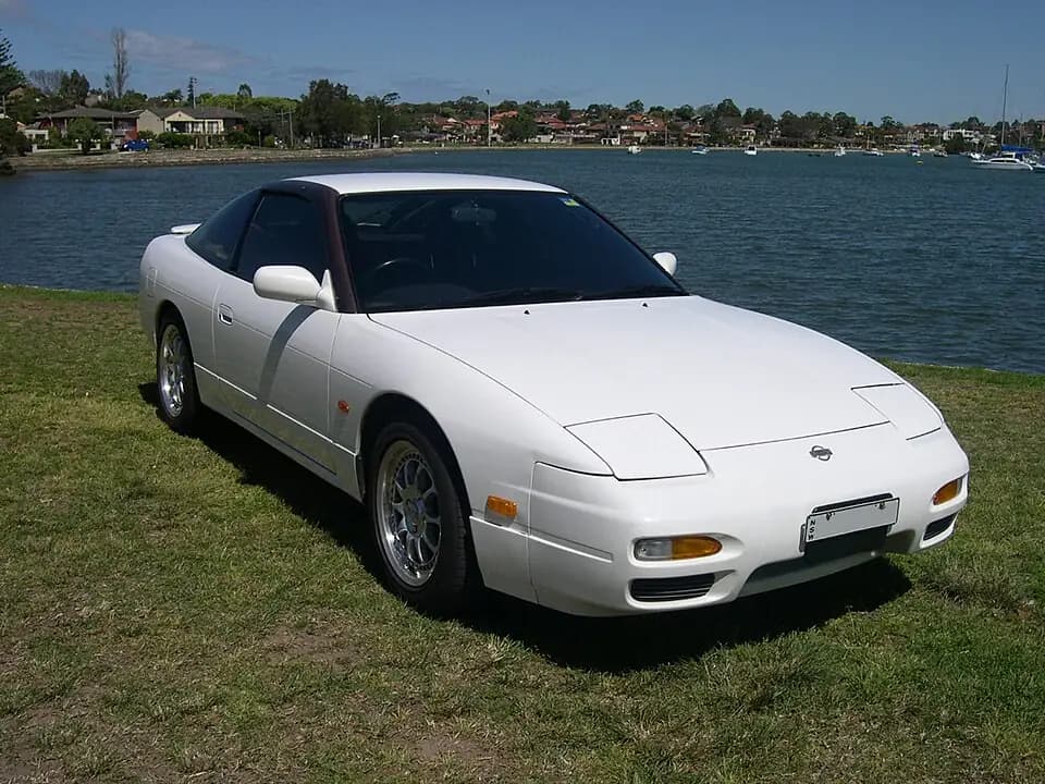White 1995 Nissan 180SX (RPS13 chuki) hatch on grass by the water, front three-quarter view