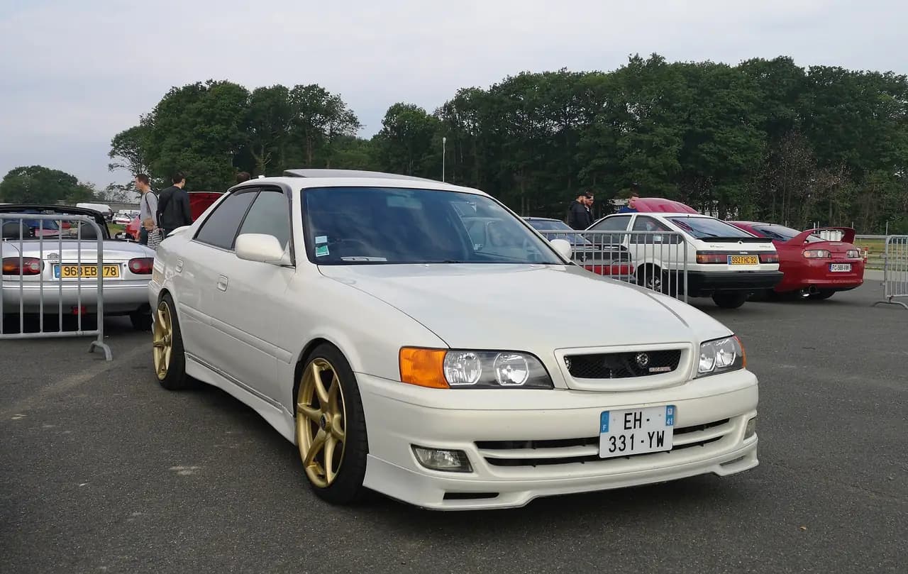 White Toyota Chaser Tourer V (JZX100) on gold aftermarket wheels, front three-quarter view