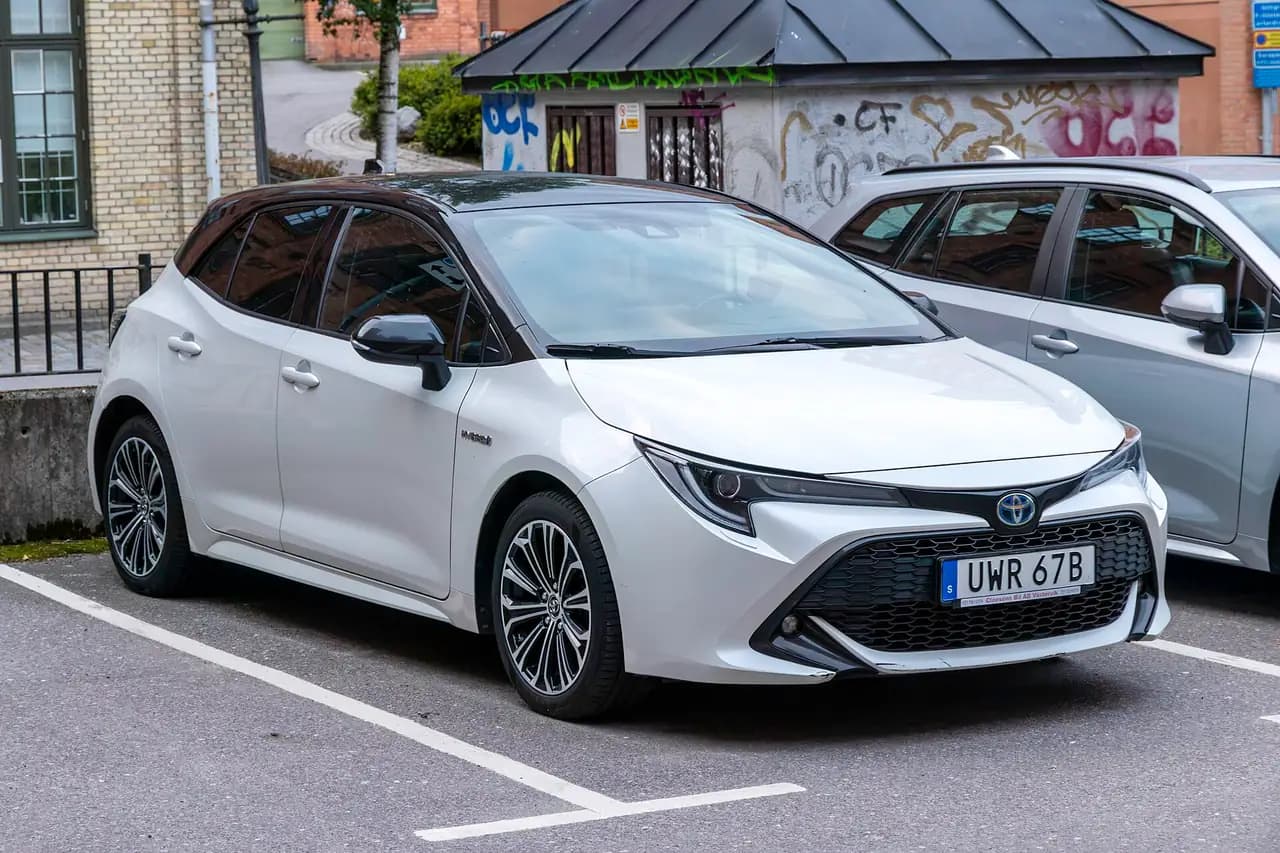 White Toyota Corolla Hybrid hatchback (E210) with black roof, front three-quarter view